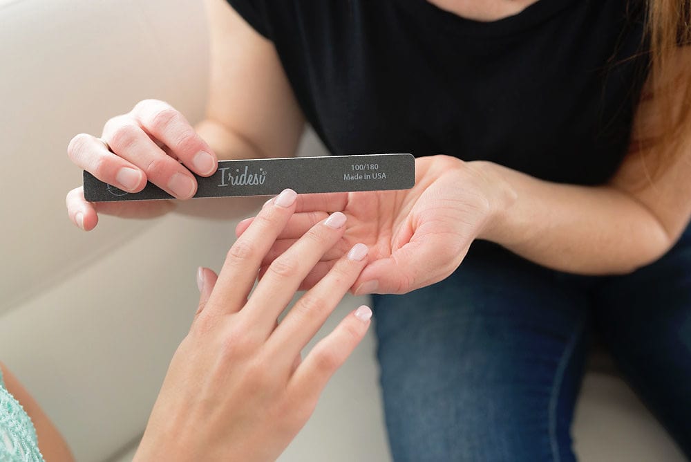 women sitting on a couch holding a black Iridesi square end nail file, filing the nail of another women's hand.