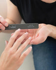 women sitting on a couch holding a black Iridesi square end nail file, filing the nail of another women's hand.
