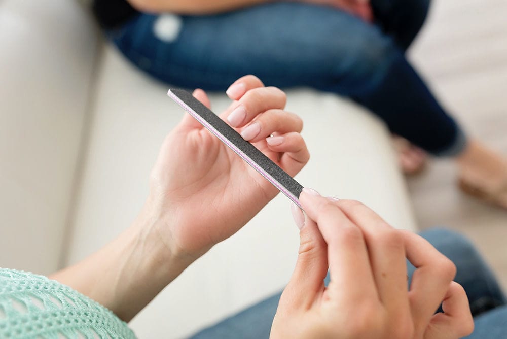 women's hands holding a black, square end nail file, while on a couch. close up