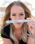 brown haired women in a black shirt holding an Iridesi zebra nail file printed with Iridesi logo, name, and grit.