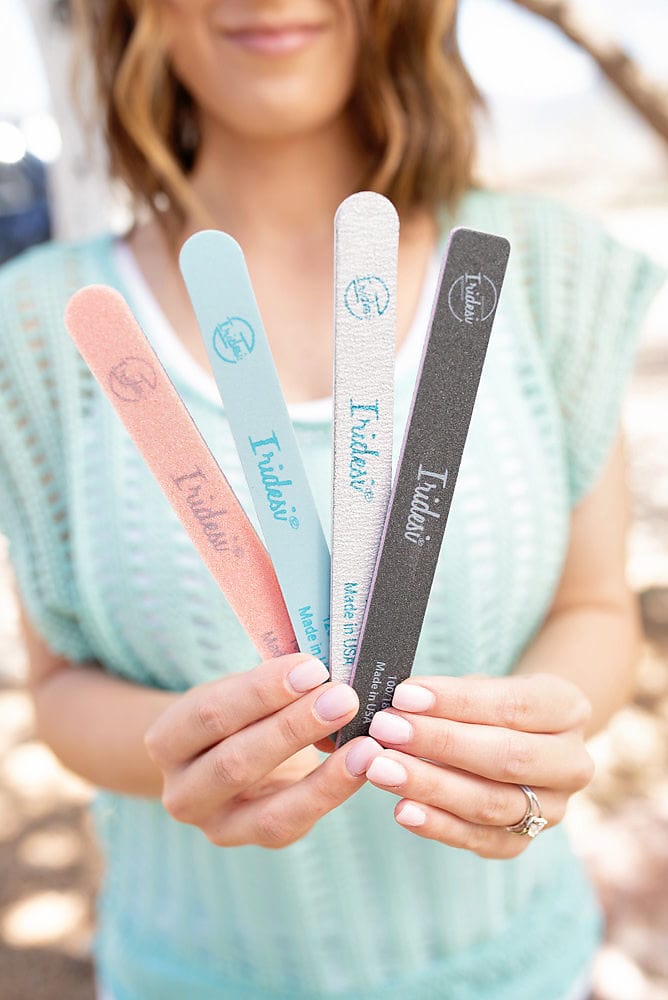 women in blue holding 4 Iridesi nail files that are printed with the logo, name and grit. From left to right orange sponge file, blue, zebra, and black. All are 7 inches long and 3/4 of an inch wide.