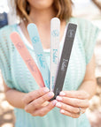 women in blue holding 4 Iridesi nail files that are printed with the logo, name and grit. From left to right orange sponge file, blue, zebra, and black. All are 7 inches long and 3/4 of an inch wide.