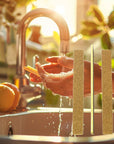 a women washes her hands at the sink in the sunlight. 3 brown nail files with a yellow center overlay the image.