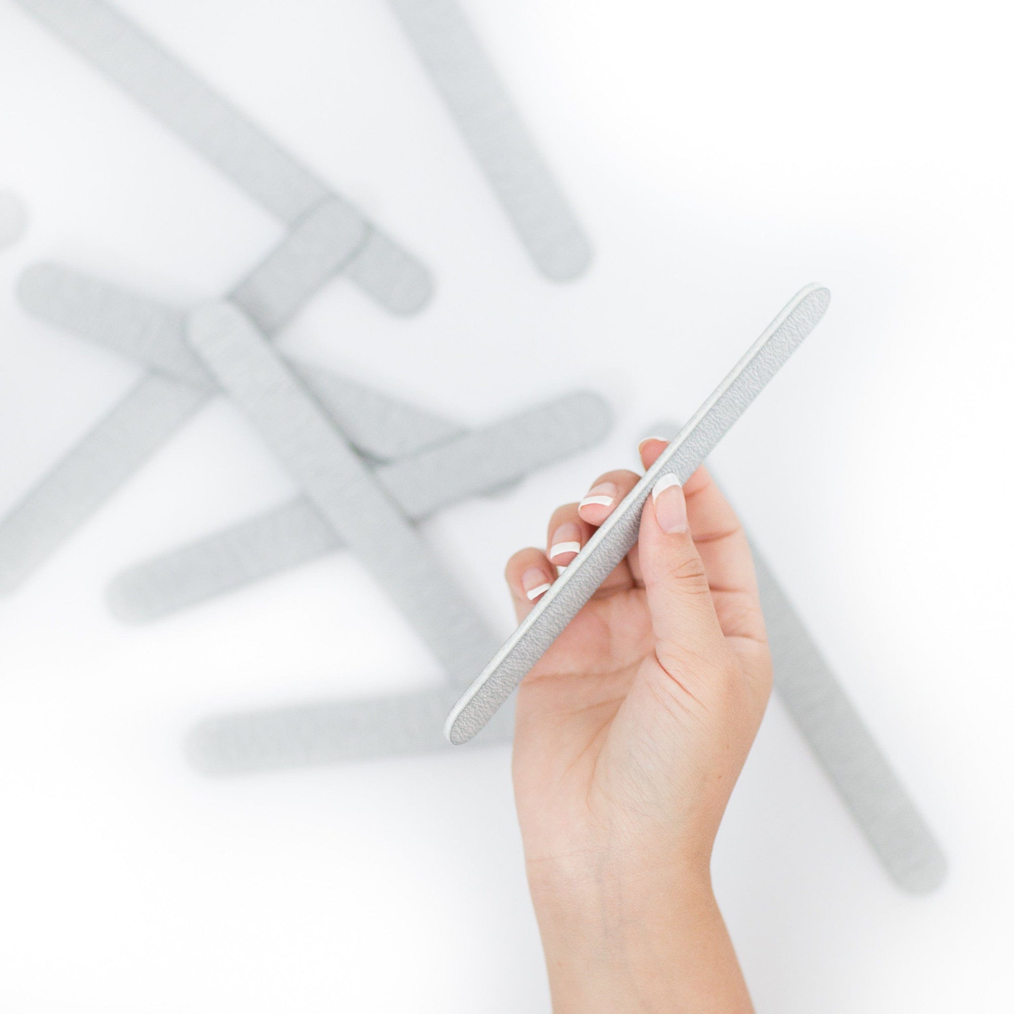 women's hand with French manicured hands holding a 7 inch zebra nail file, white center. The background more scattered zebra nail files out of focus.