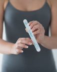 Zebra nail file in a women's hand wearing a grey tank top. Iridesi name, logo and grit printed on the nail file.