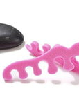 Teenie toe separators. Pink toe separators in the shape of a baby foot. White background. smooth black rock near toe separators.