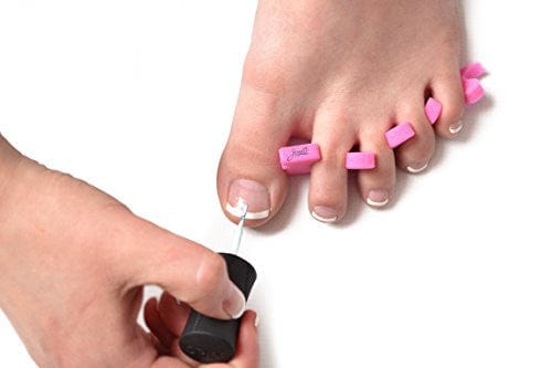 women's foot with the teenie toe separators on with a French pedicure. White background. Another women's hand applying a clear coat of nail polish.