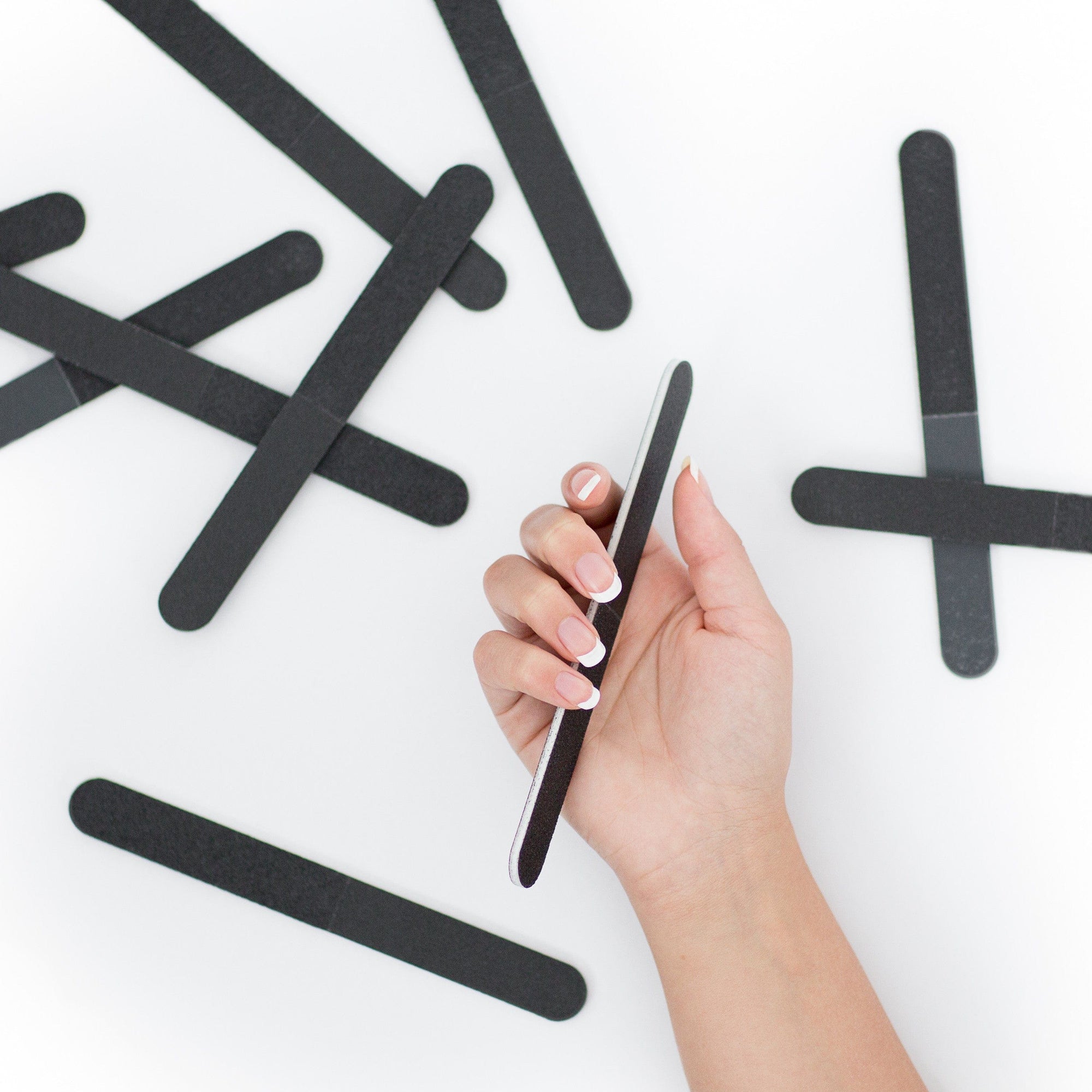 women's hand holding a black 4 way nail file, white center, round edges, white background, some scattered in the background.