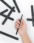 women's hand holding a black 4 way nail file, white center, round edges, white background, some scattered in the background.